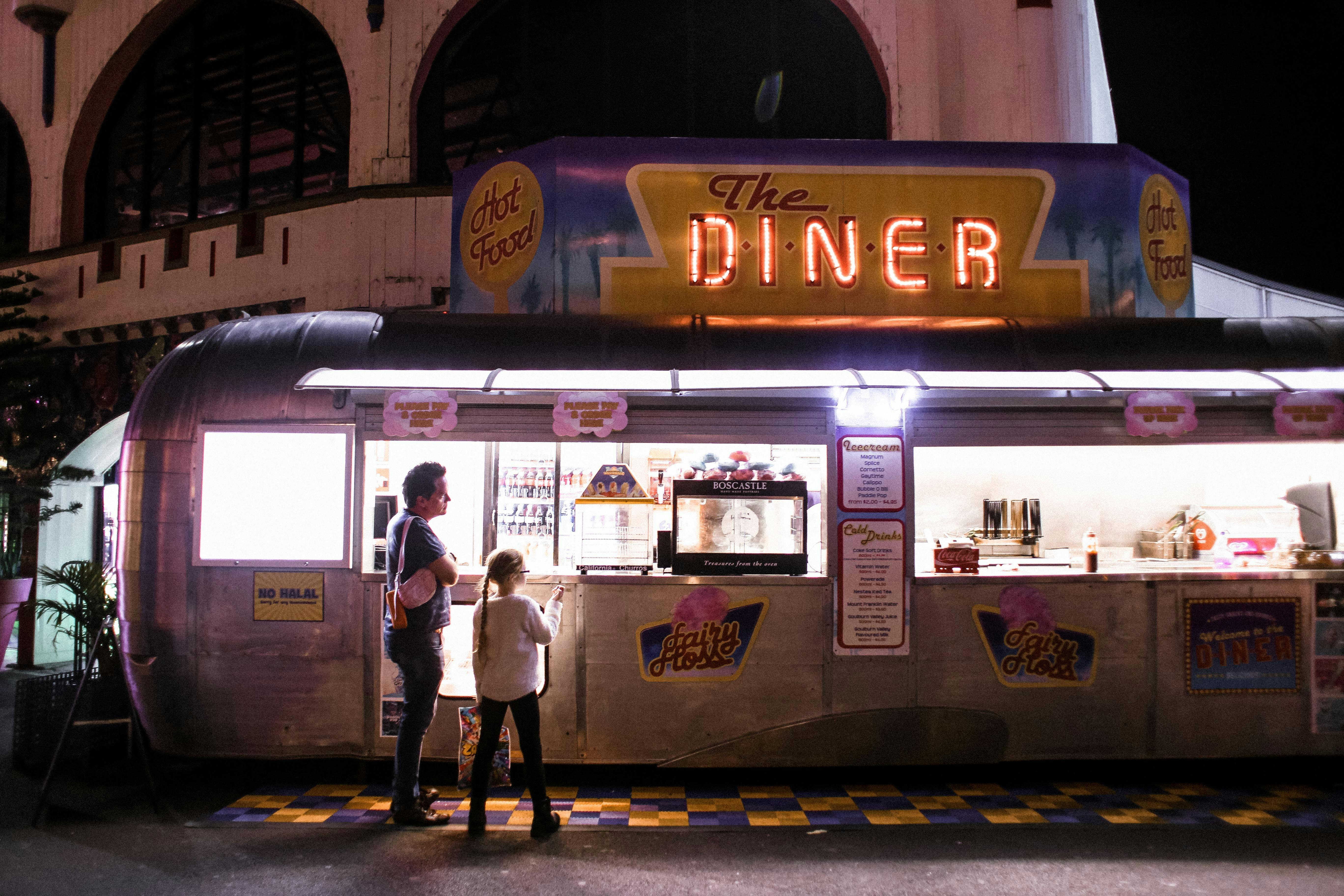 Evening scene with a father and daughter ordering at a neon-lit retro diner food truck.
