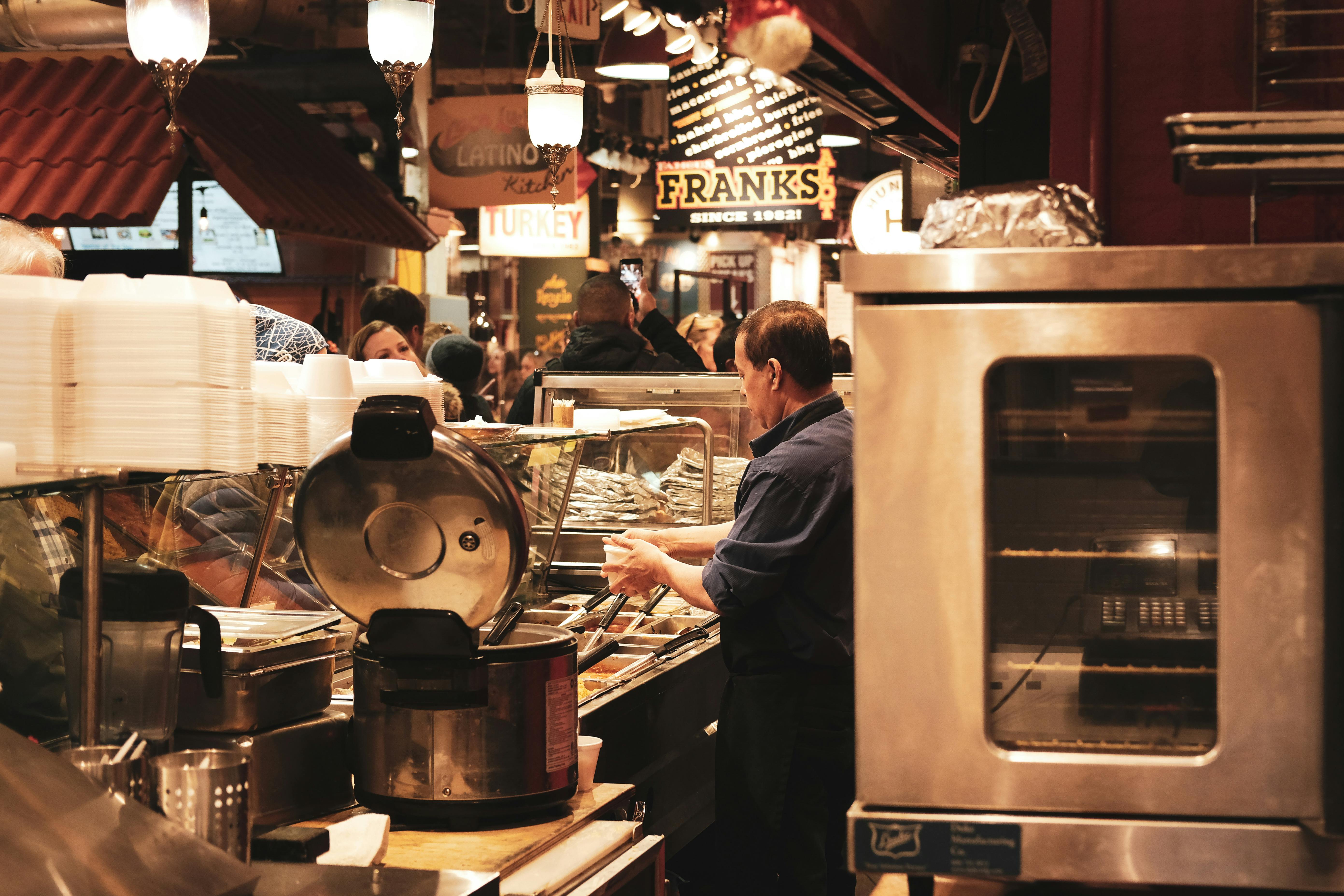 A busy food hall with a man preparing food, showcasing bustling market activity.